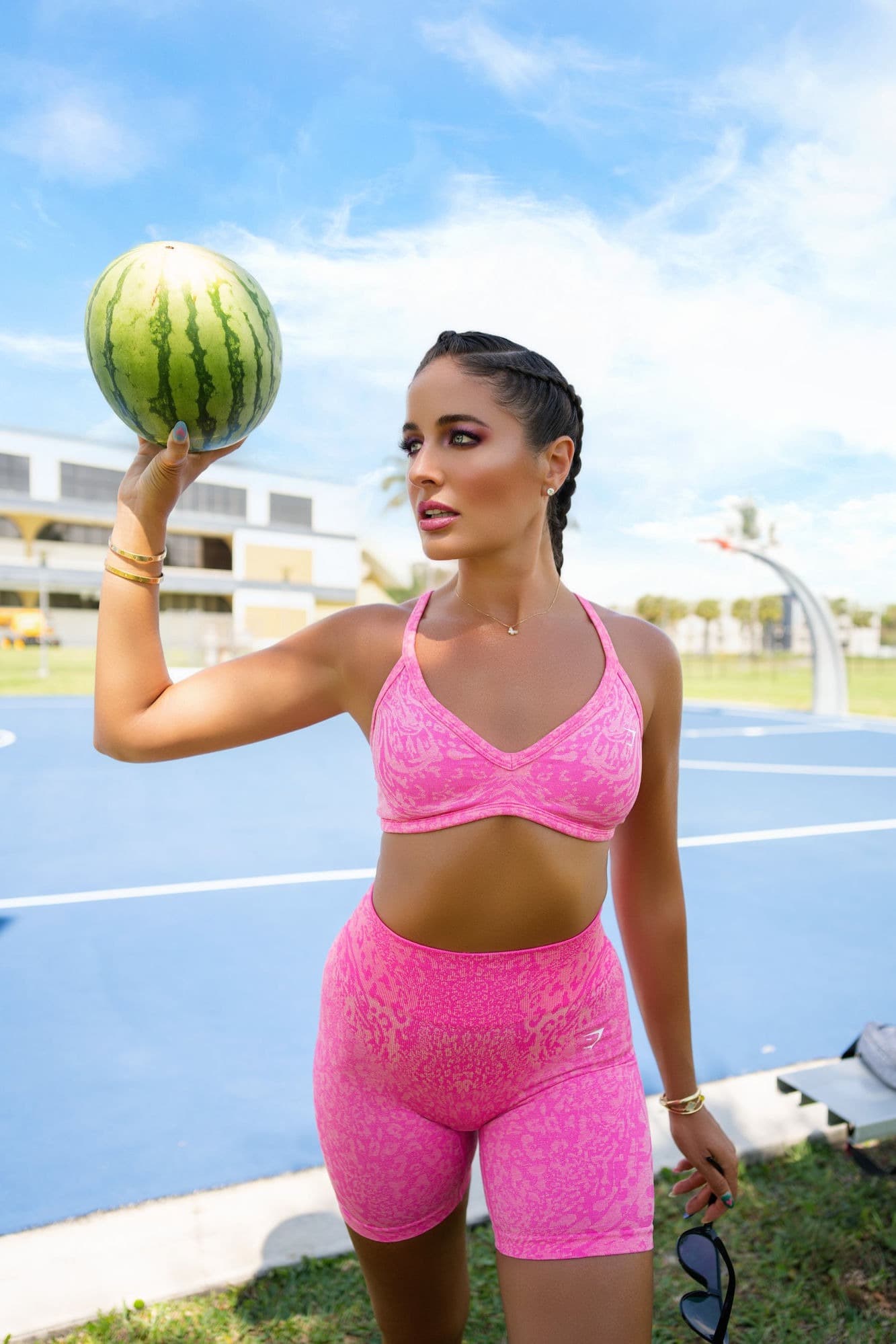 Charlotte in pink activewear balancing a watermelon on a sunlit basketball court