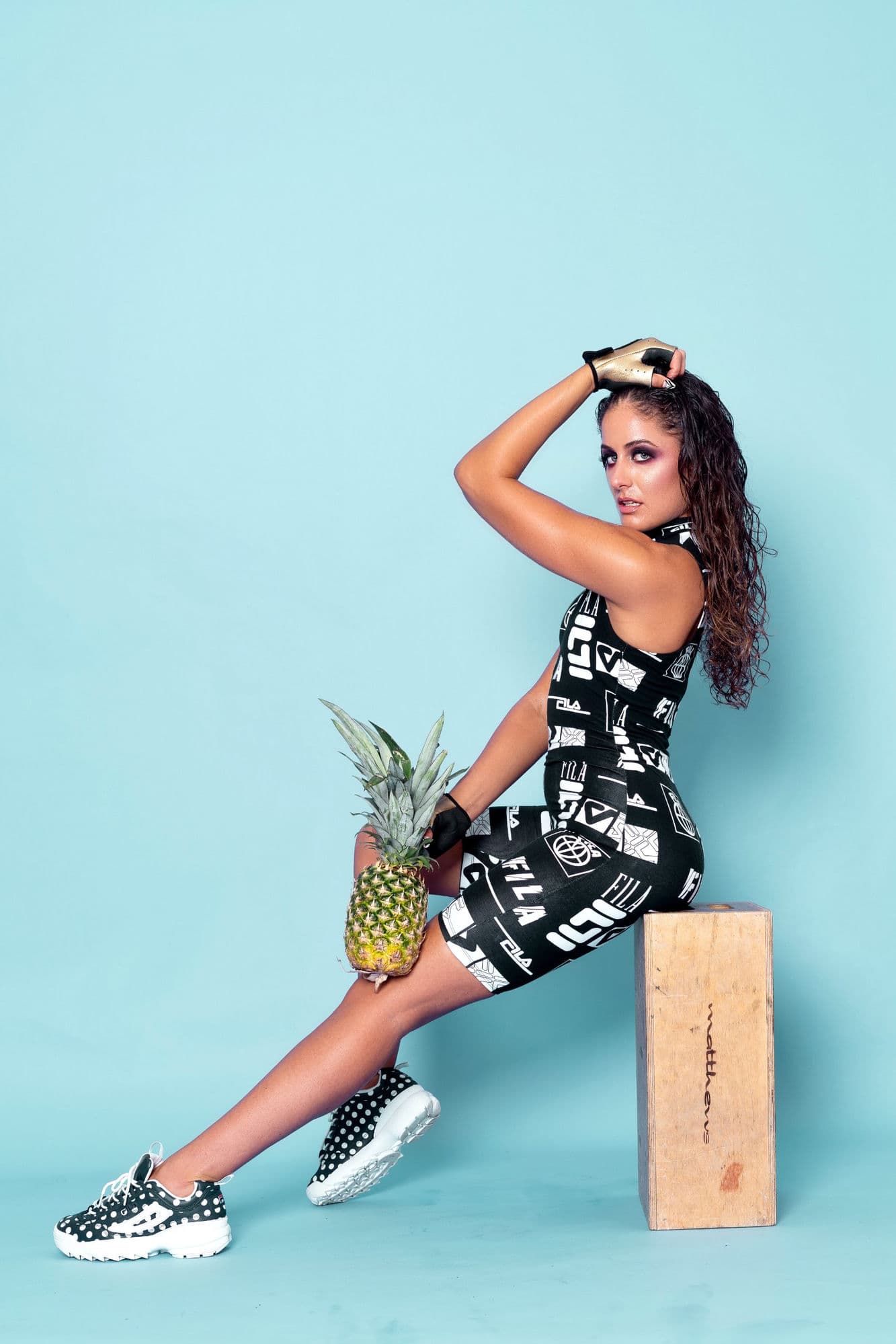 Charlotte in a bold black-and-white print bodysuit seated against a teal studio backdrop with a pineapple