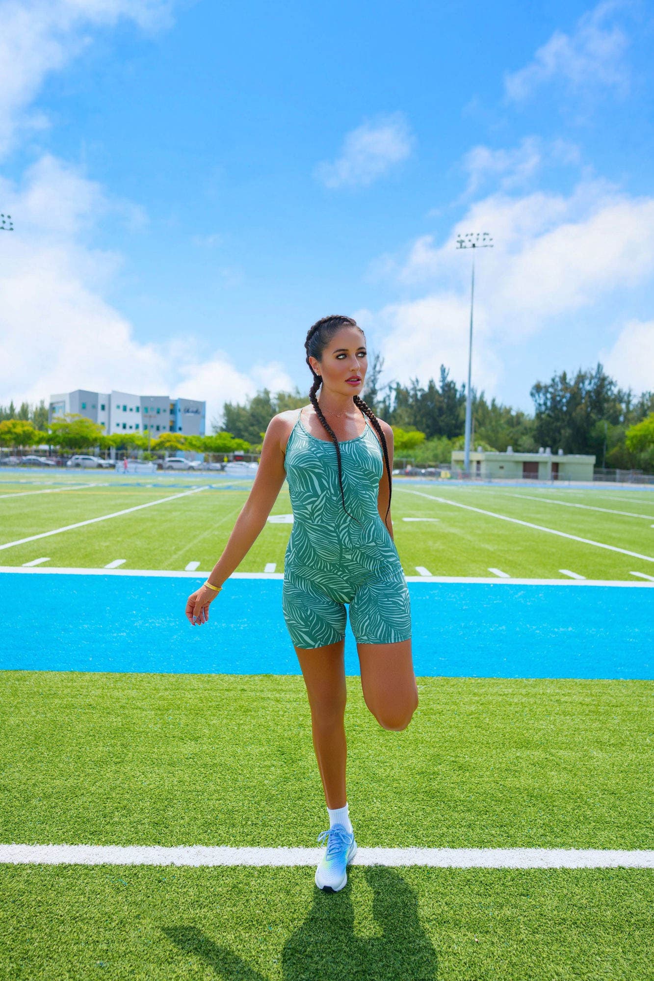 Charlotte walking across a sunlit turf field in a palm-print romper