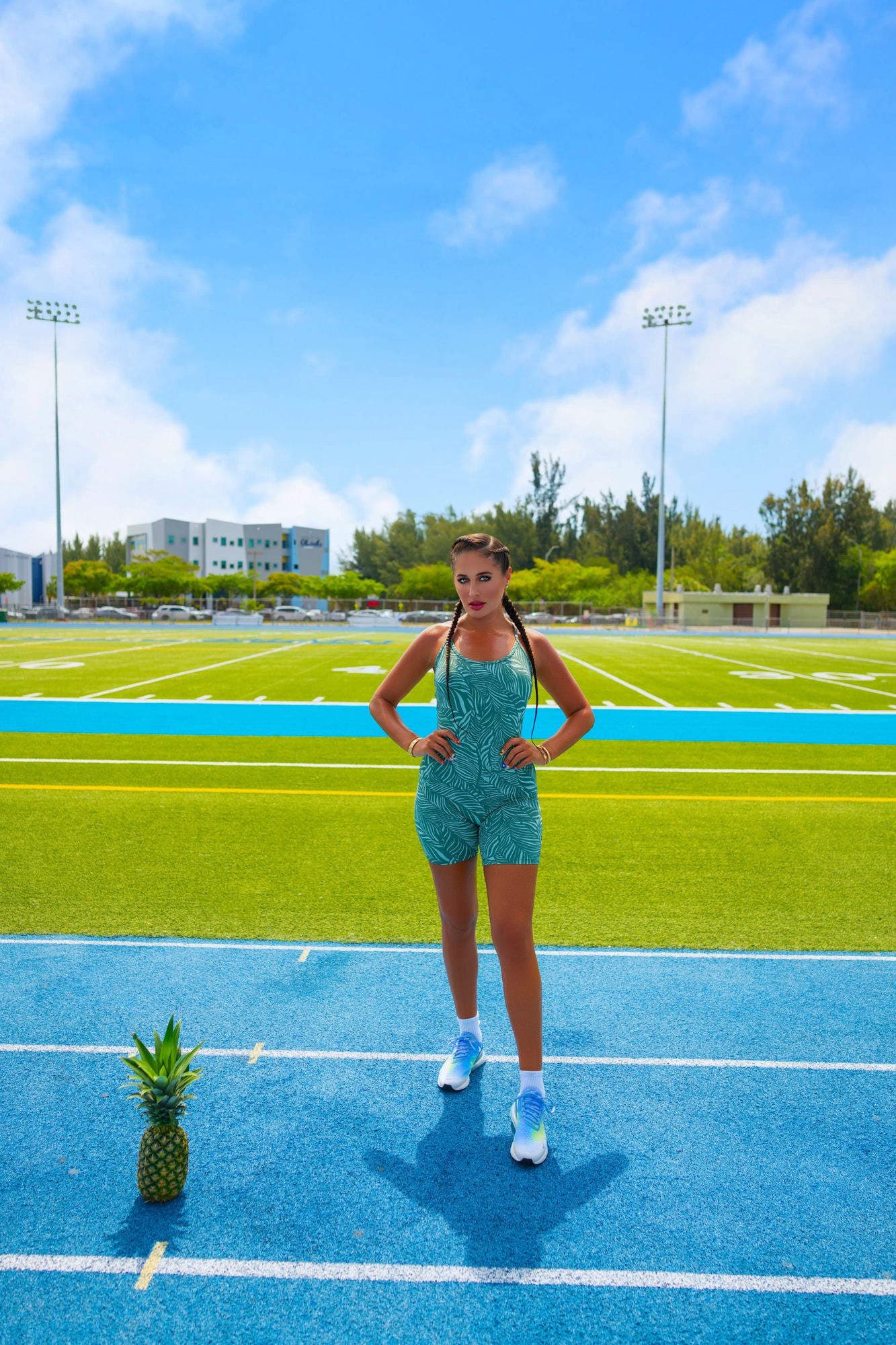 Charlotte standing tall, hands on hips, on a blue running track with a football field behind her