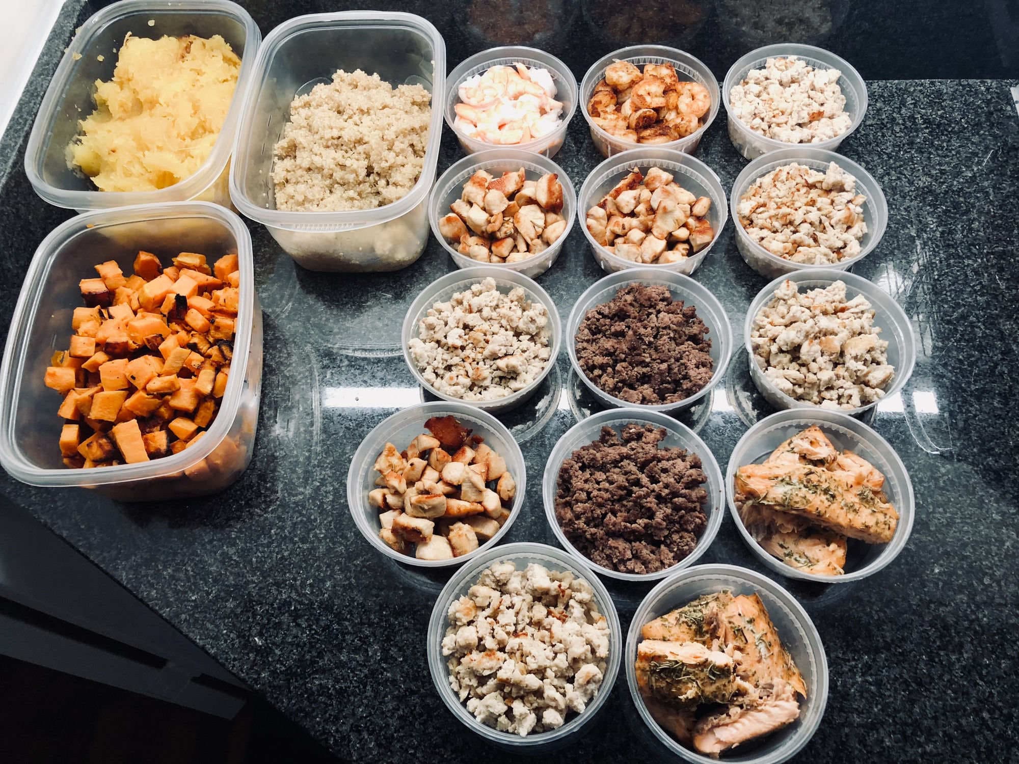 A full spread of meal-prep containers — proteins, quinoa, sweet potato and shrimp — portioned for the week